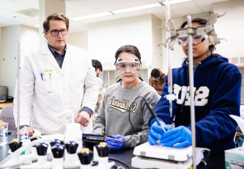 Two students wearing St. Edward's sweatshirts and a professor in a lab coat work in an analytical experiments lab.